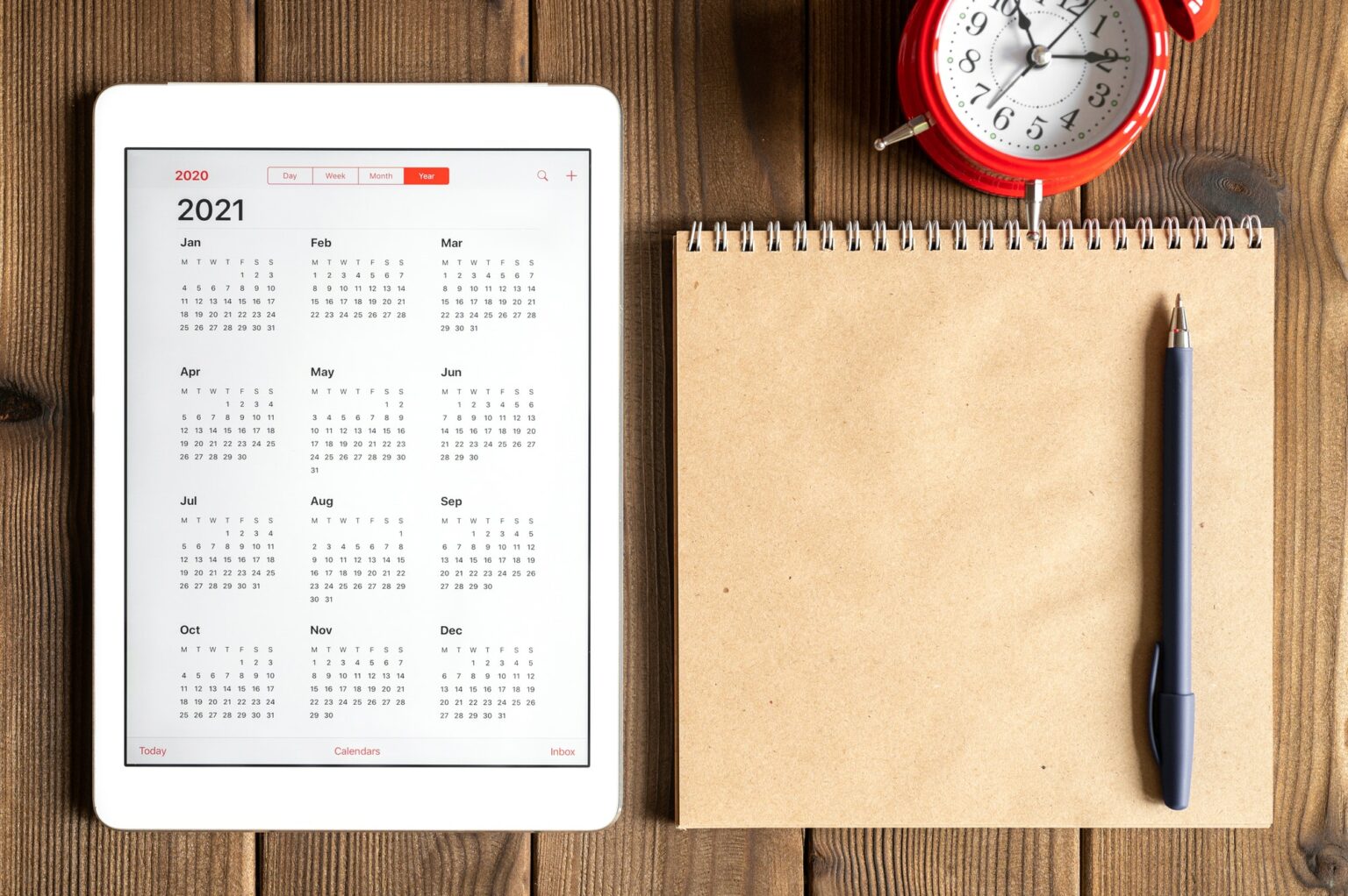 tablet with calendar for 2021, alarm clock and a craft paper notebook on a wooden background
